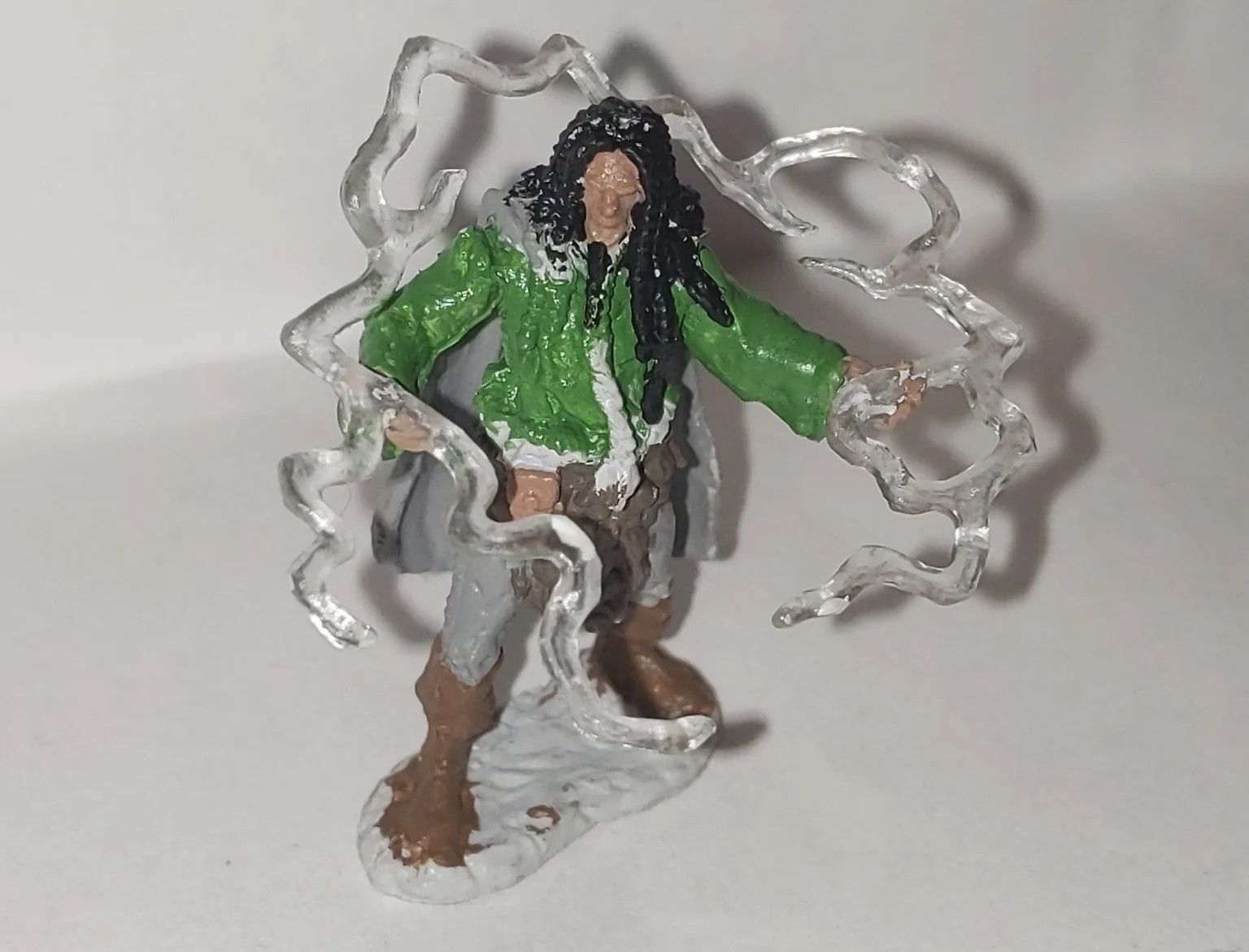 Miniature figure of a person with long black hair and a green jacket, emitting translucent energy.