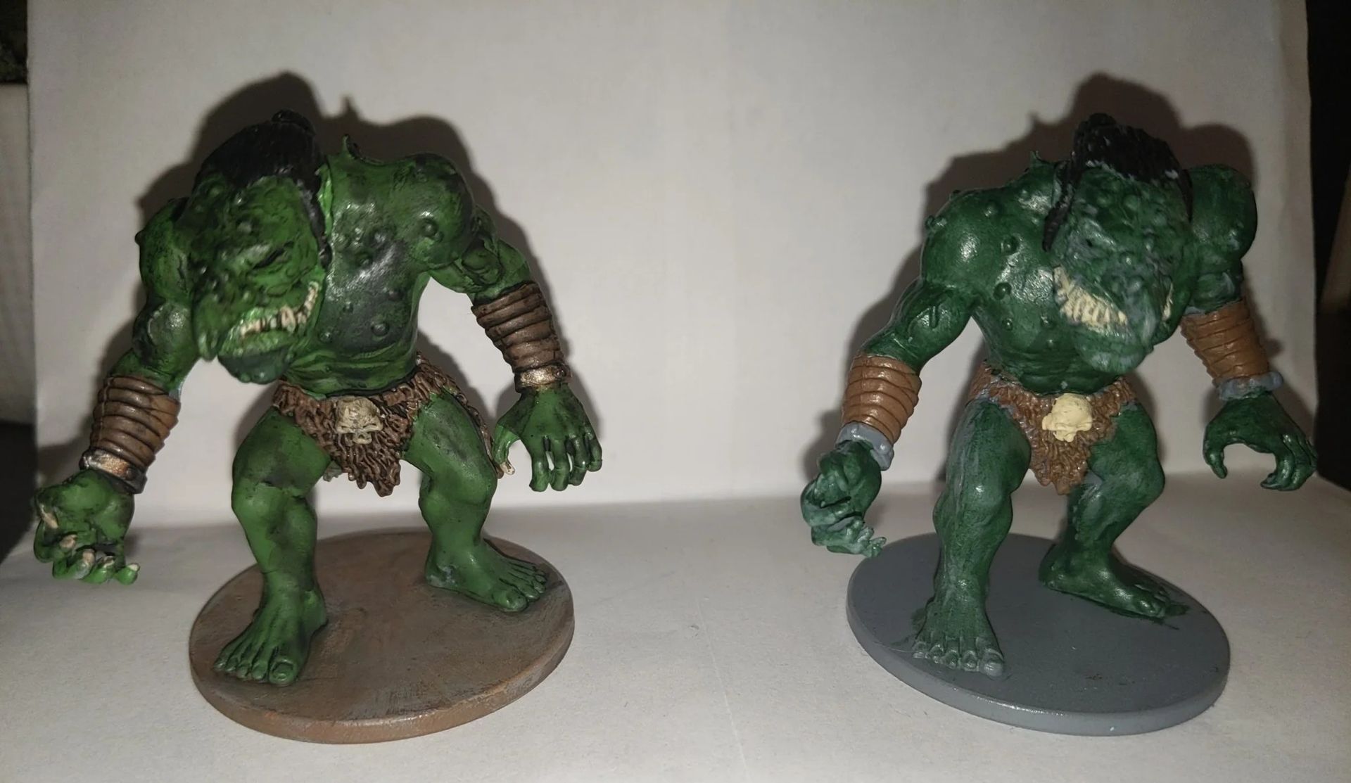 Two green troll figurines, one on a brown base, the other on a gray base.