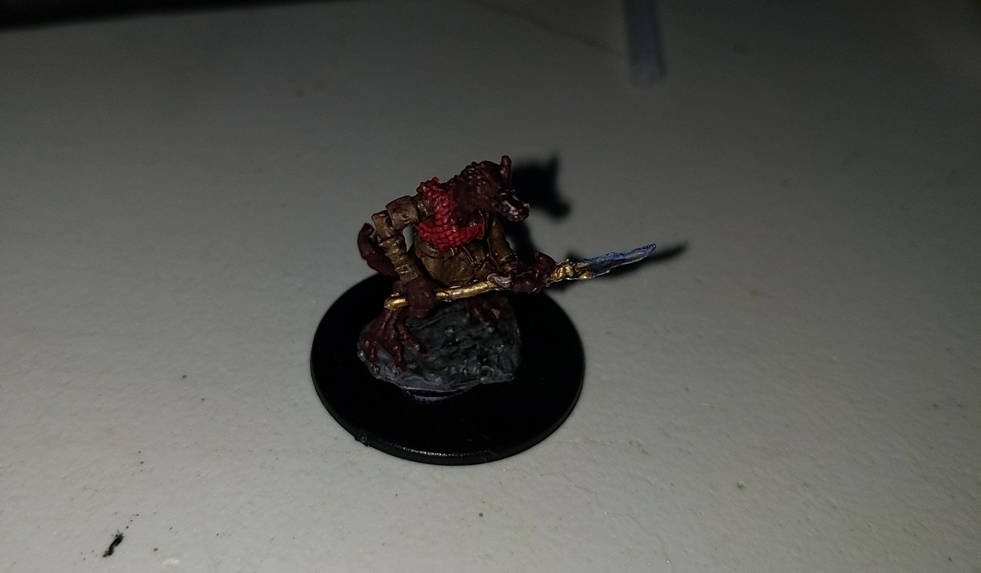 Miniature figure of a warrior with red and gold armor, on a black base.