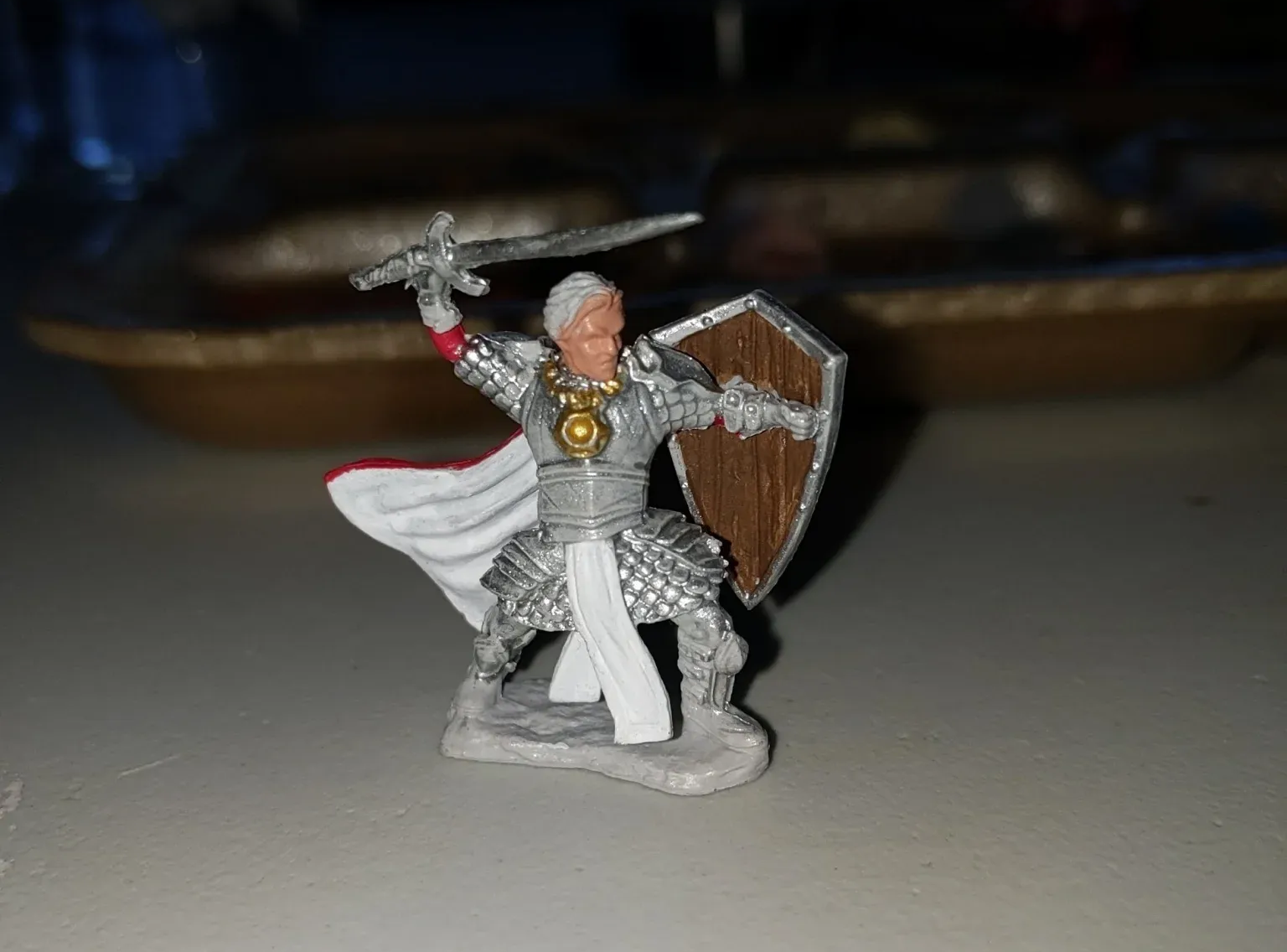 Miniature figure of a knight in silver armor, holding a sword and shield, in a defensive stance.