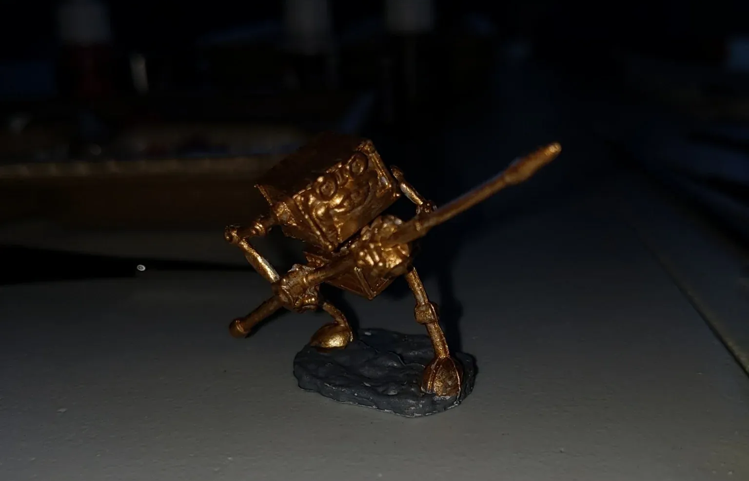 Gold-colored miniature cannon on a black base, set against a blurry background.