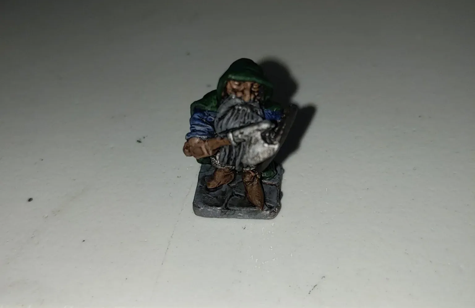 Miniature figurine of a dwarf wearing a green hat and blue shirt, holding a shield and weapon.