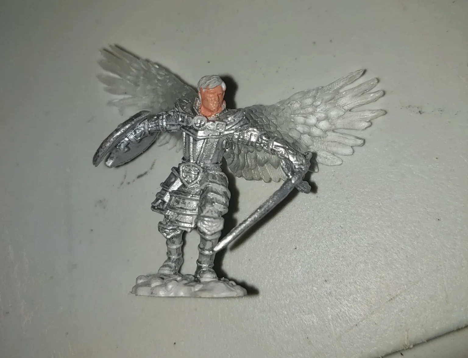 Miniature angel warrior figure with silver armor, white wings, and sword.