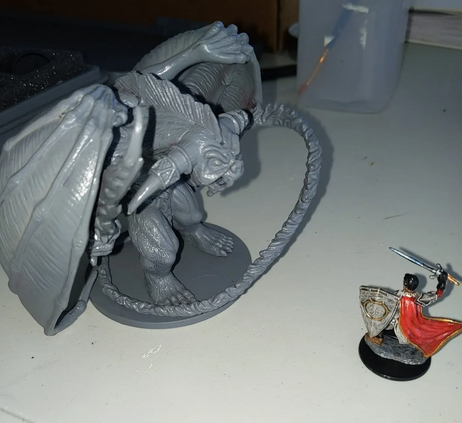 A large, unpainted monster miniature and a painted miniature of a figure with a sword on a white surface.