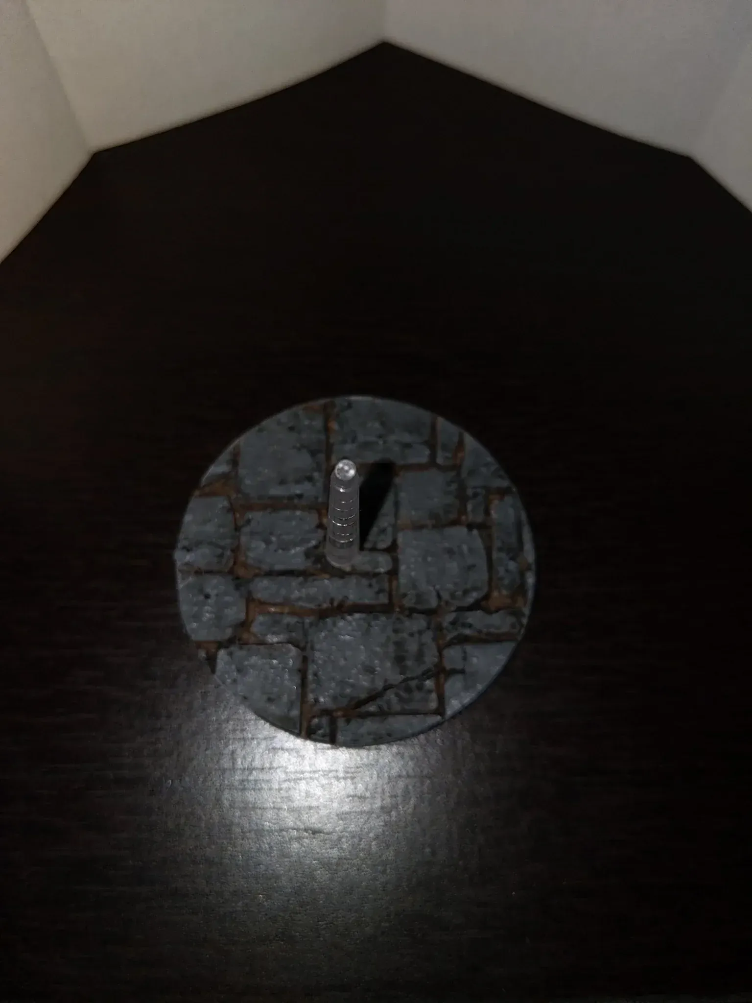 Round, stone-textured base with a metallic, rectangular piece in the center, on a dark surface.
