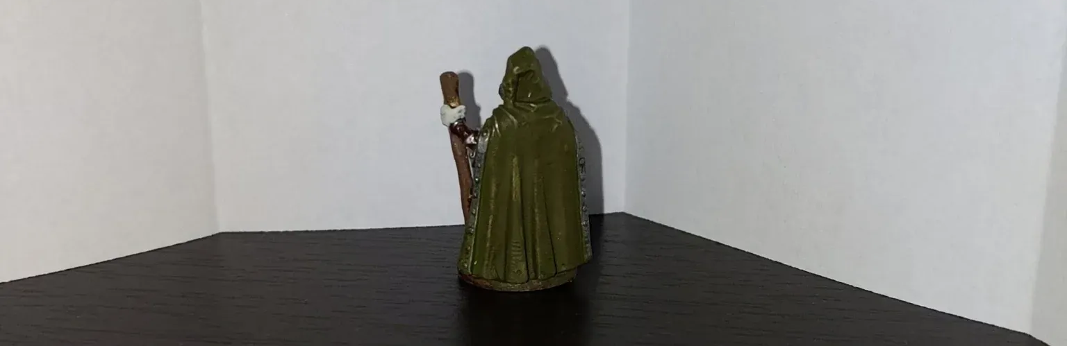 A green-robed figure with a staff stands on a black surface against a white wall.