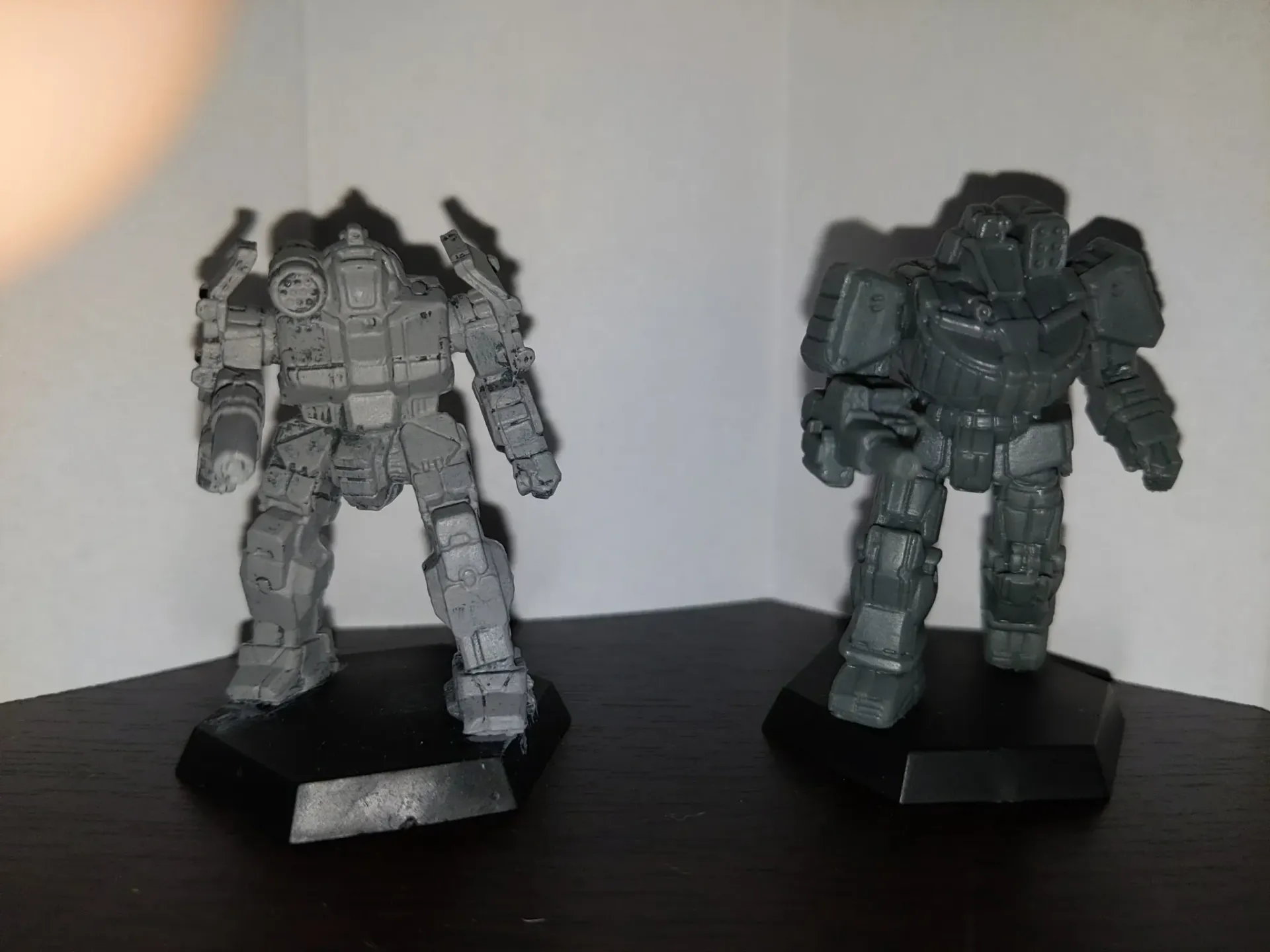 Two gray robot miniatures on black bases stand on a shelf.