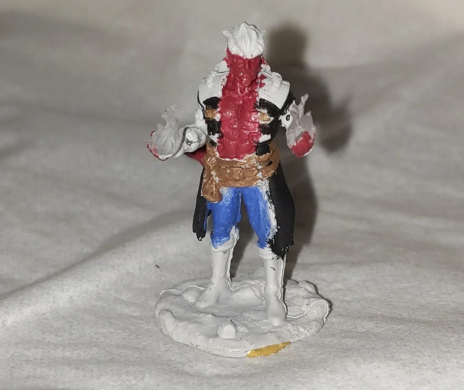 Miniature figure of a character with red and white mask, black coat, blue pants, on white surface.