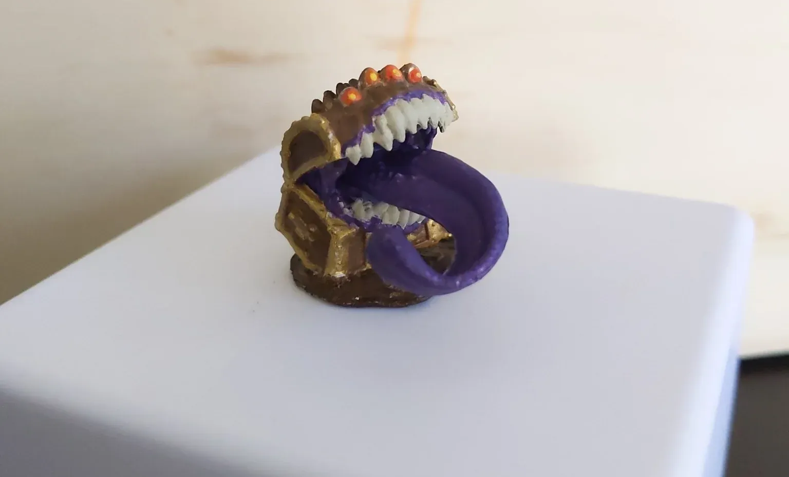 A miniature, gold-colored mimic chest with a gaping mouth, purple tongue, and sharp teeth.