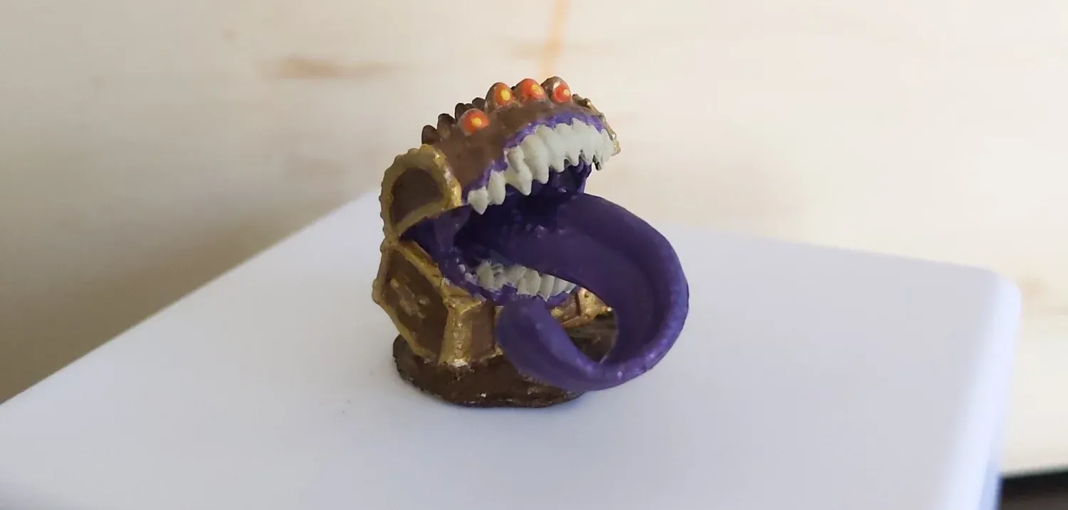 Mimic miniature figurine: gold chest with sharp teeth, long purple tongue.