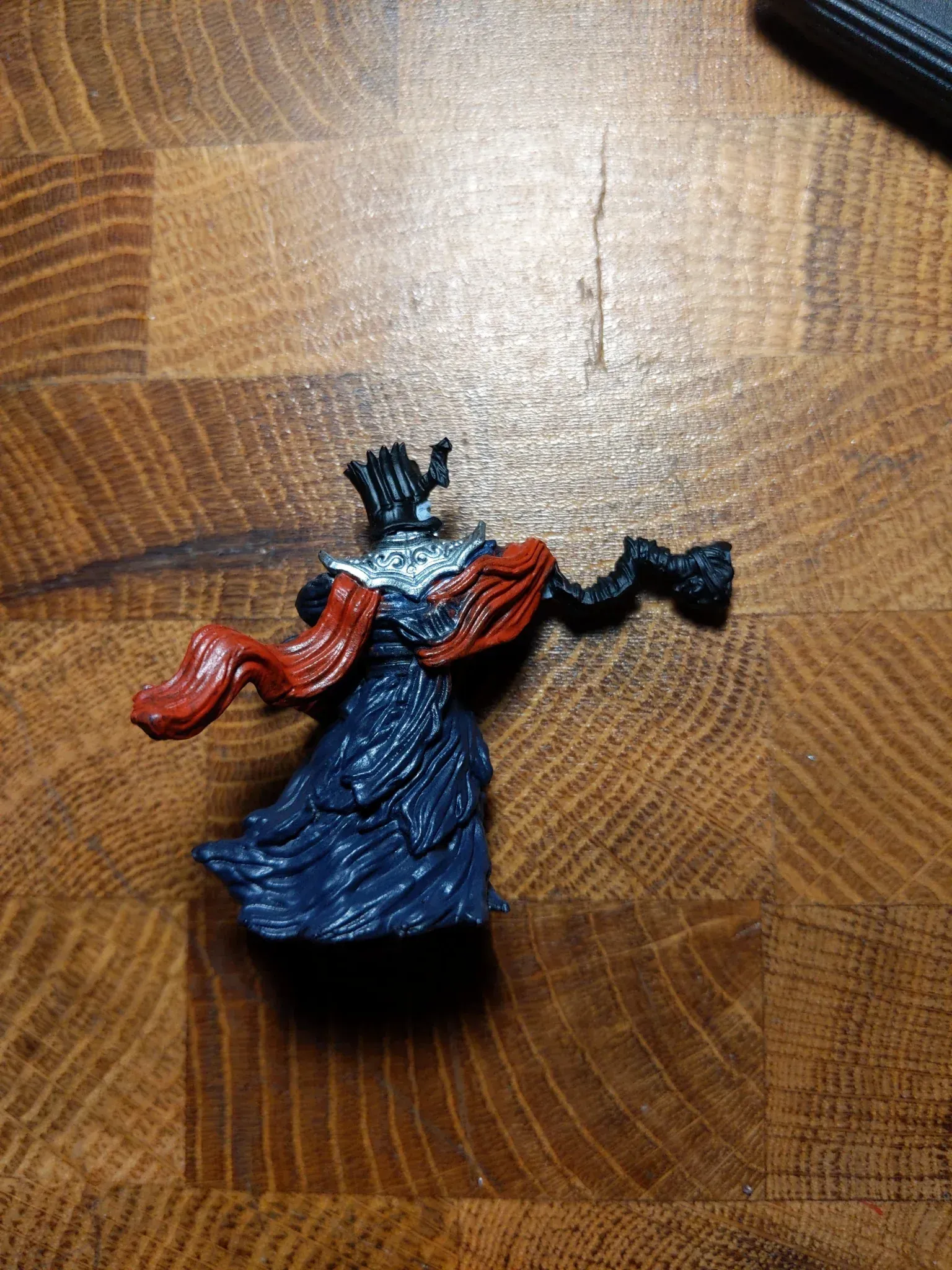 Miniature figure of a queen in blue robes and a crown, red scarf, and outstretched arm on a wood grain surface.