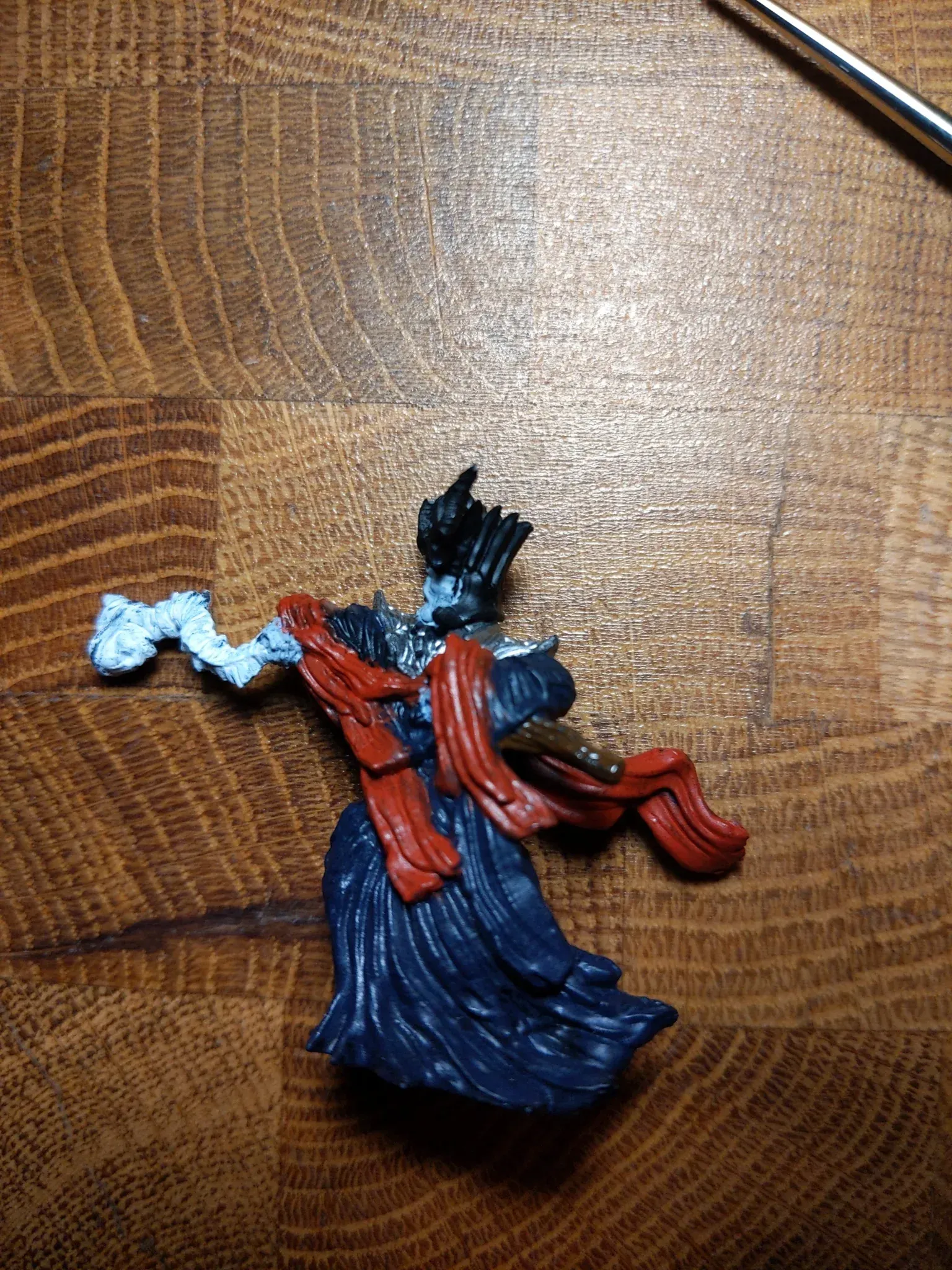 Miniature figure of a robed, blue-clad person with a red scarf, holding a white-painted arm.