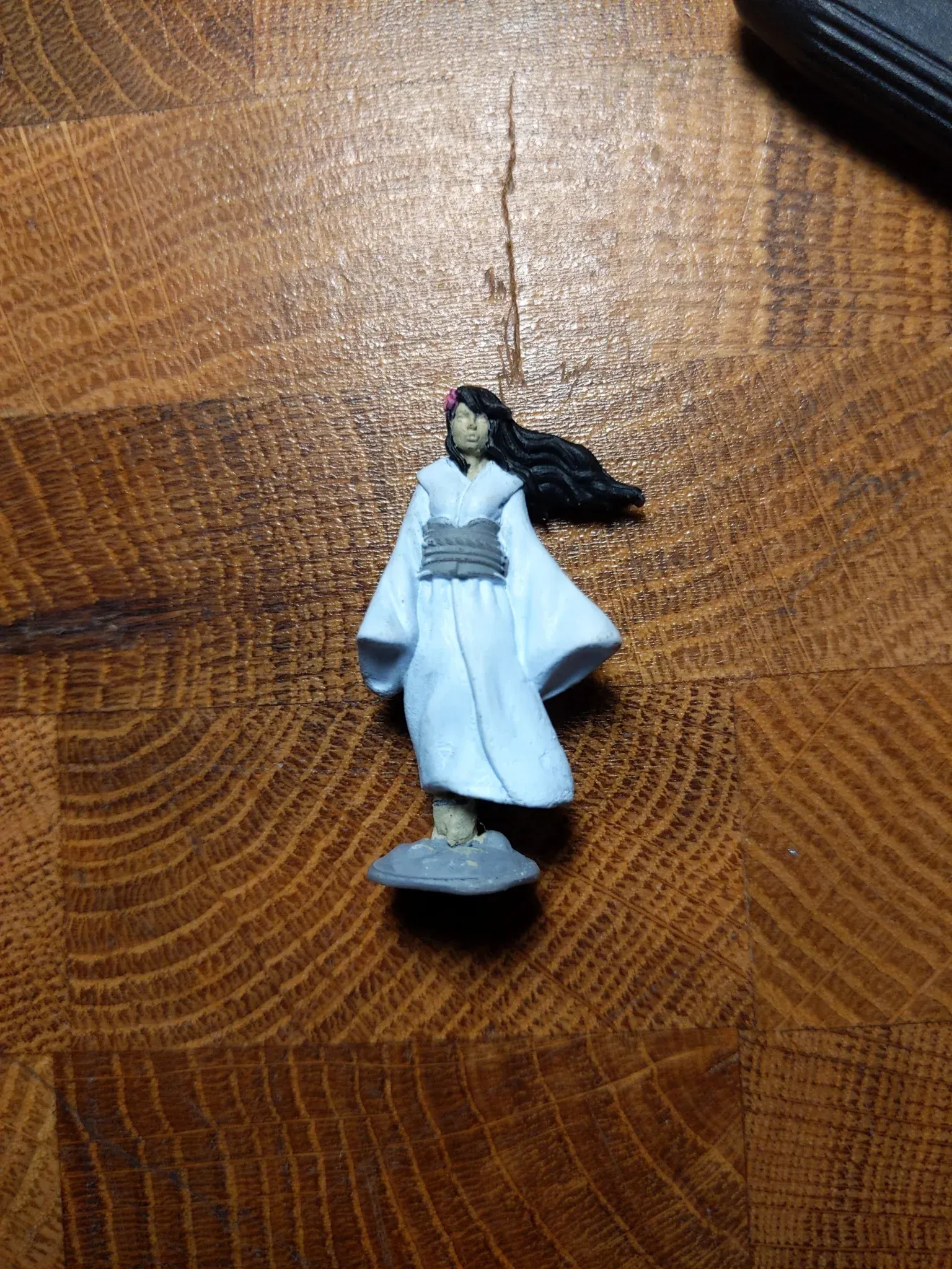 Miniature figure of a woman in a white kimono, standing on a grey base, on a wood table.