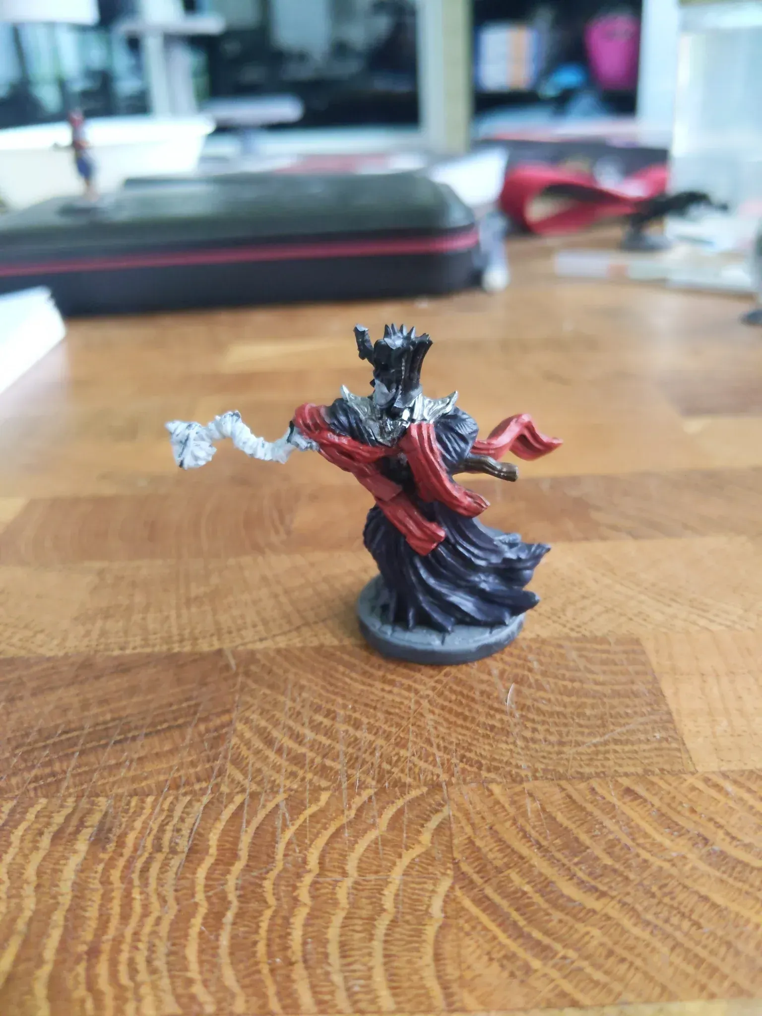 Miniature of a black robed king with a crown and red sash, posed on a wooden table.