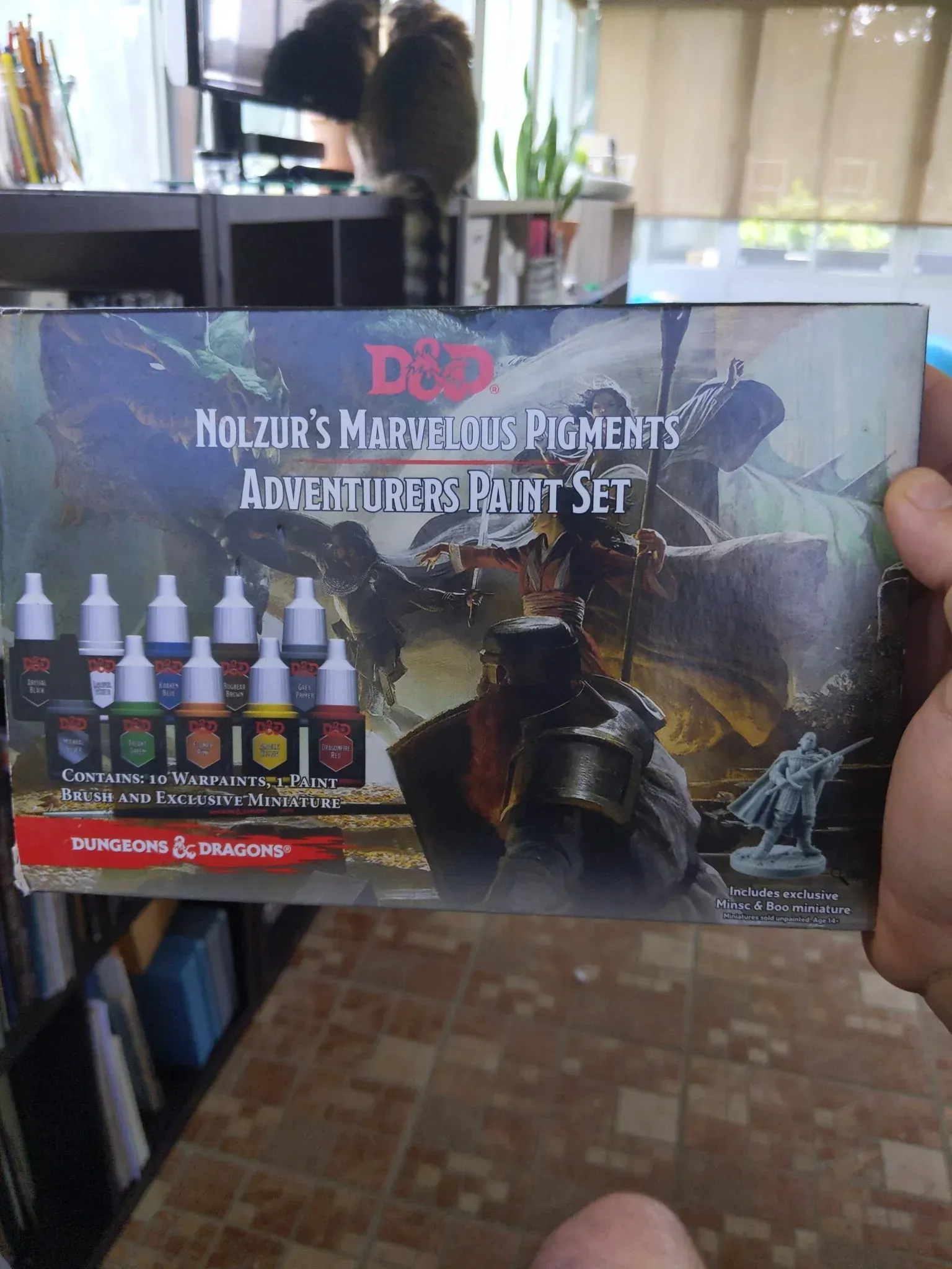 D&D Nolzur's Marvelous Pigments Adventurers Paint Set, held by a person, with paints and miniature.
