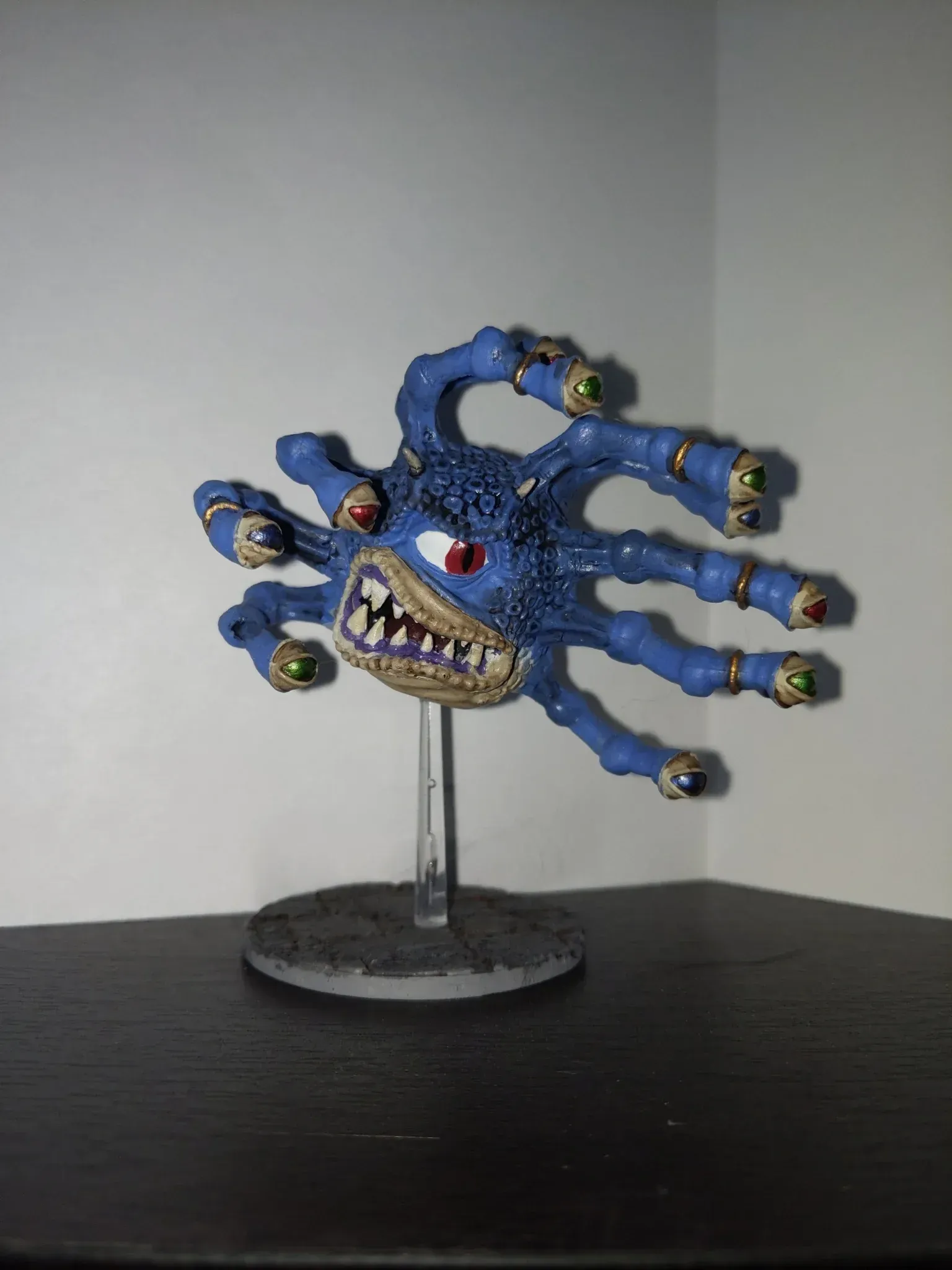 Blue, monstrous creature with many eyes, teeth, and tentacles, painted miniature on a stand.