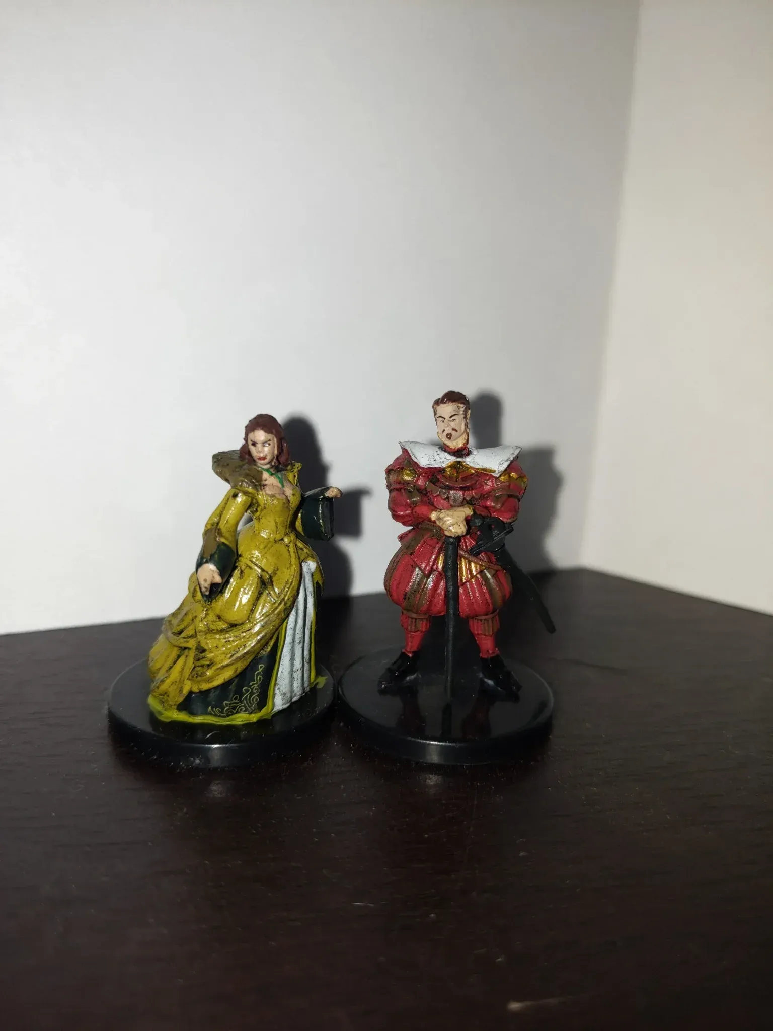 Two miniature figures: a woman in a yellow gown and a man in a red suit.