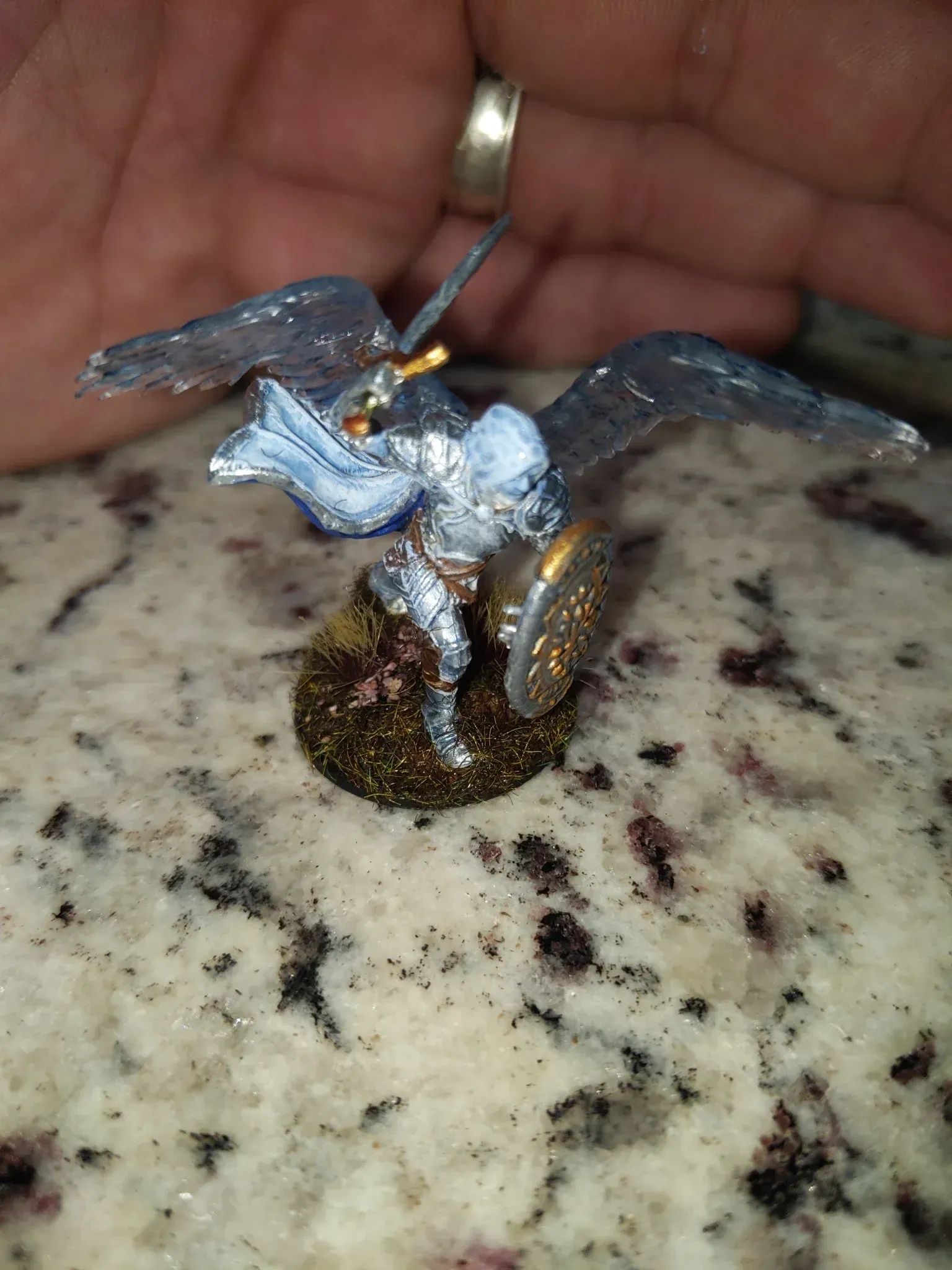 Miniature silver knight with black wings wielding sword and shield, on a glittery base.