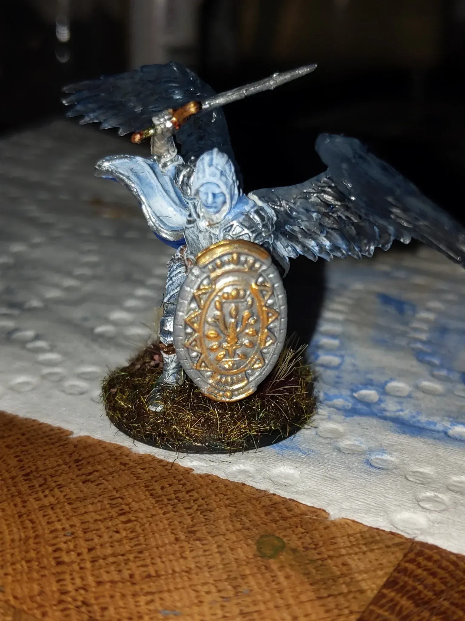 Miniature angel warrior figurine with sword and shield, wings outstretched, standing on grassy base.