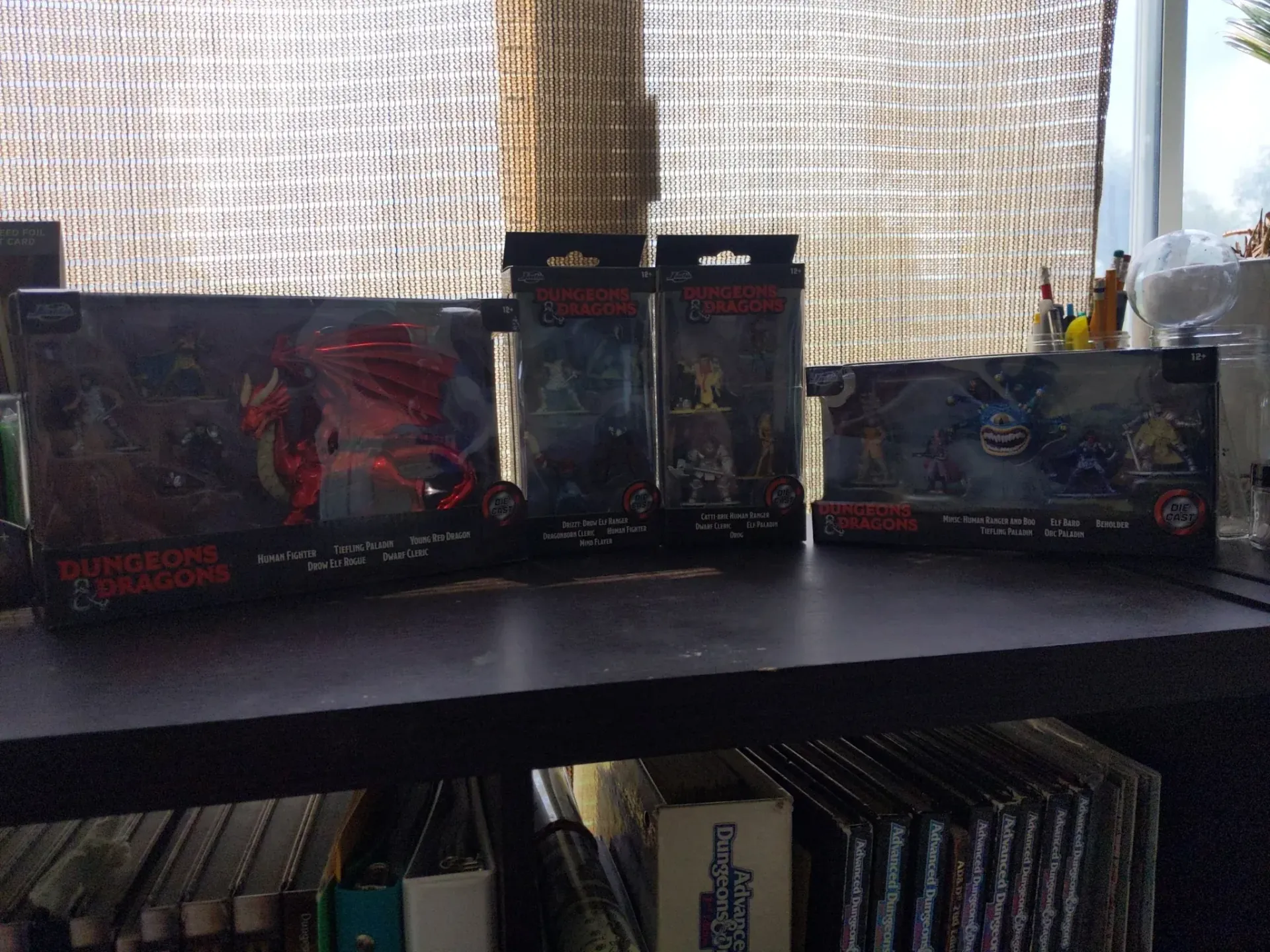 Boxes of Dungeons & Dragons miniatures on a shelf, including a red dragon, in a room.