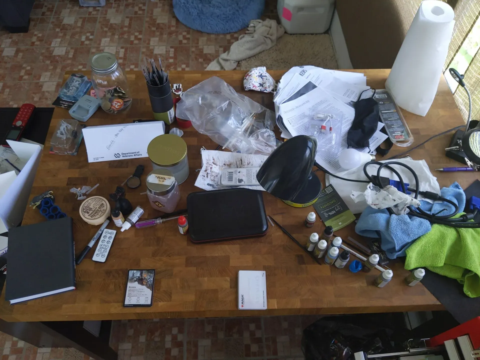 Messy wooden table with various objects including jars, a notebook, and a black purse.