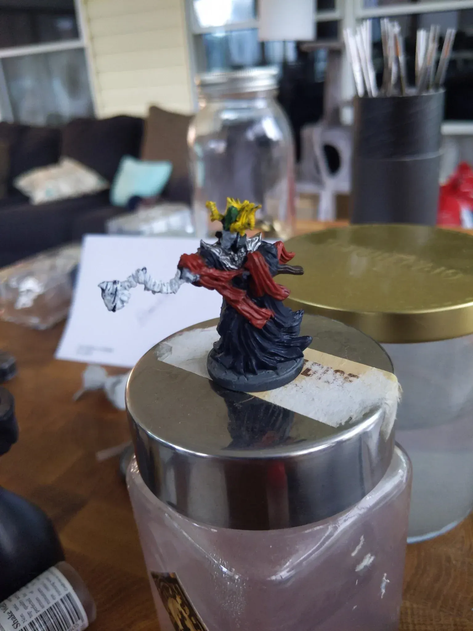 Miniature figurine, dark robes, gold crown, holding staff, on a jar lid.