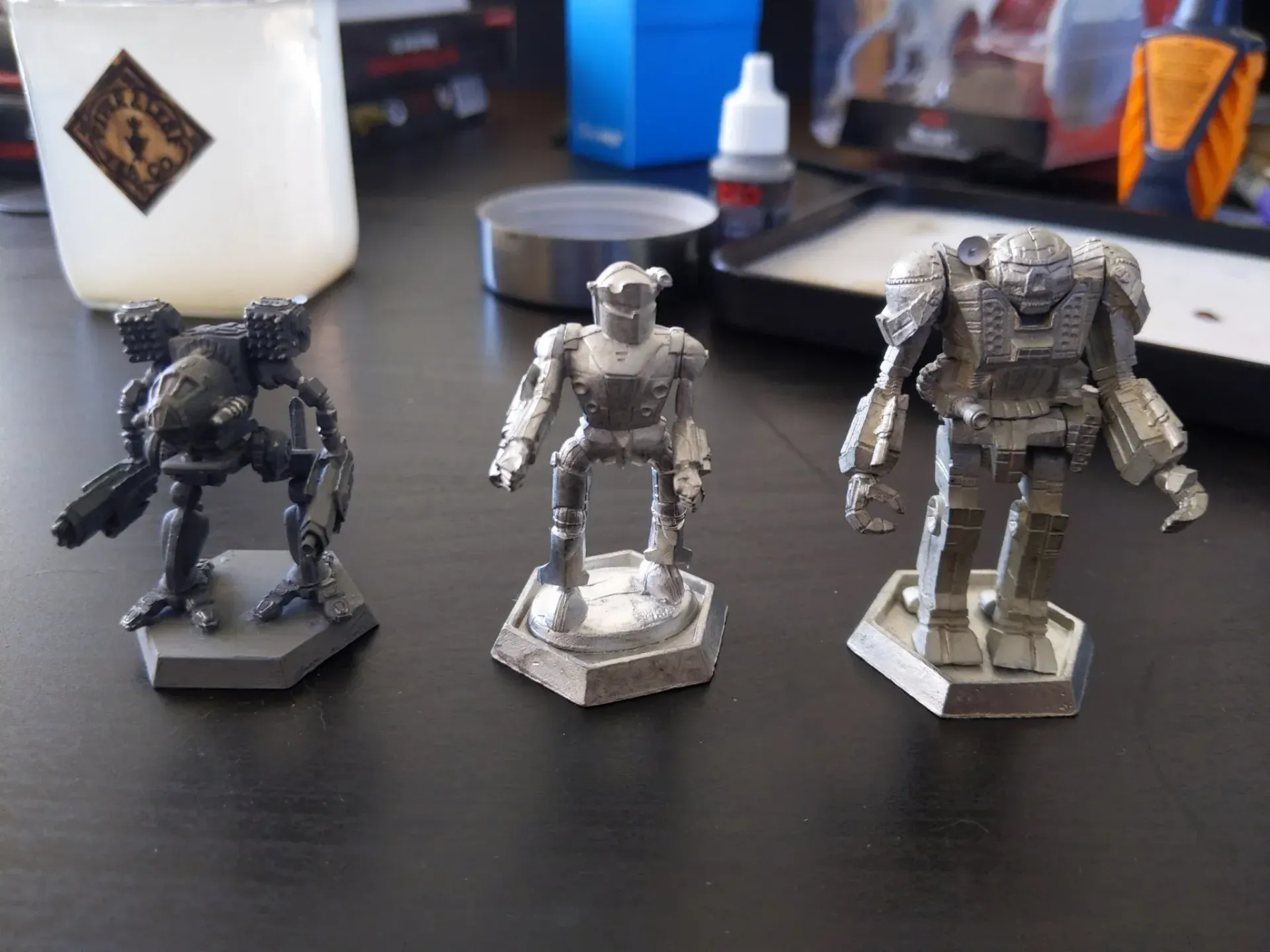 Three metal robot miniatures on a dark surface, ready for painting.