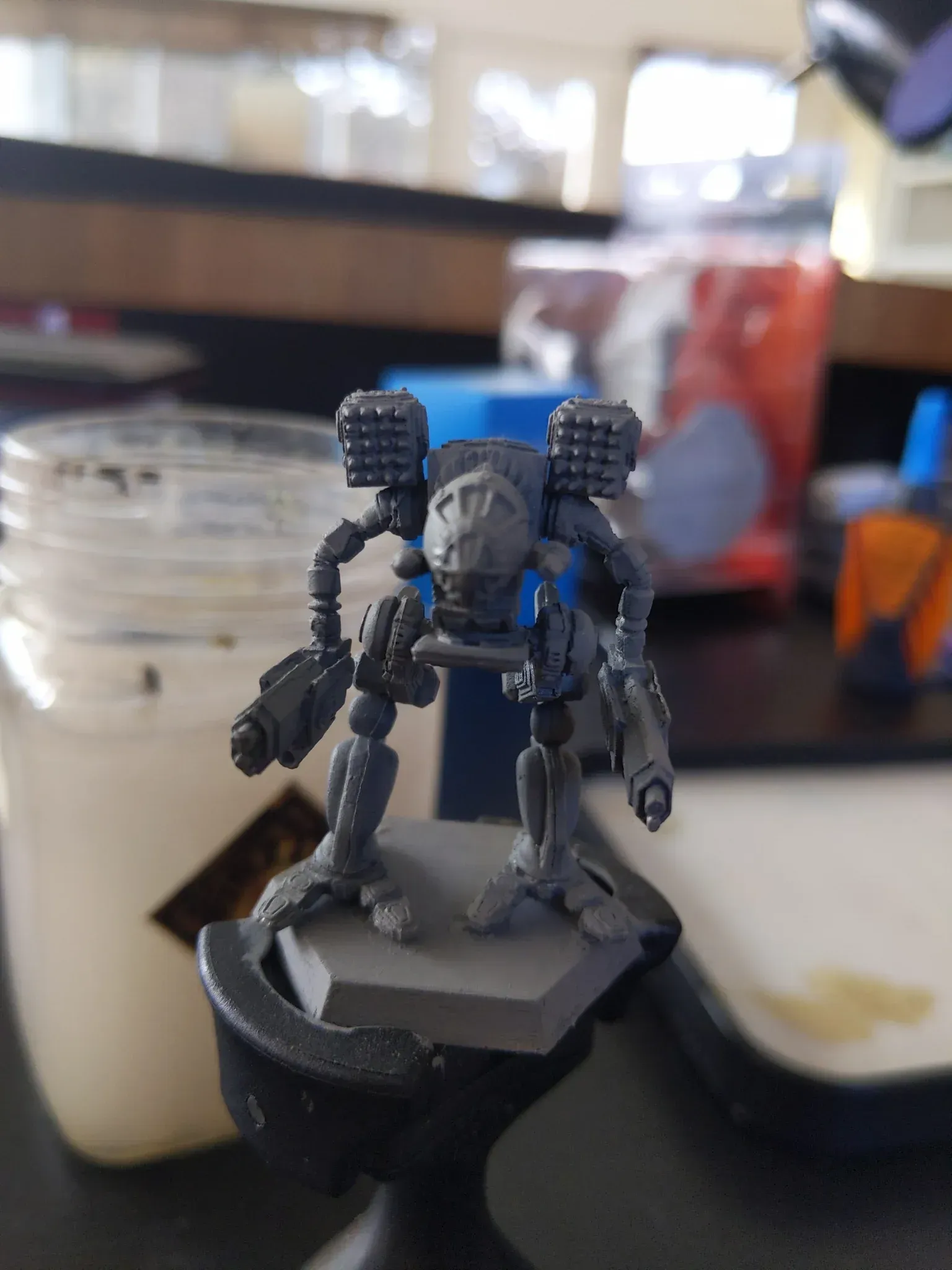 Miniature gray robot with blue highlights on a hexagonal base, held in a clamp.