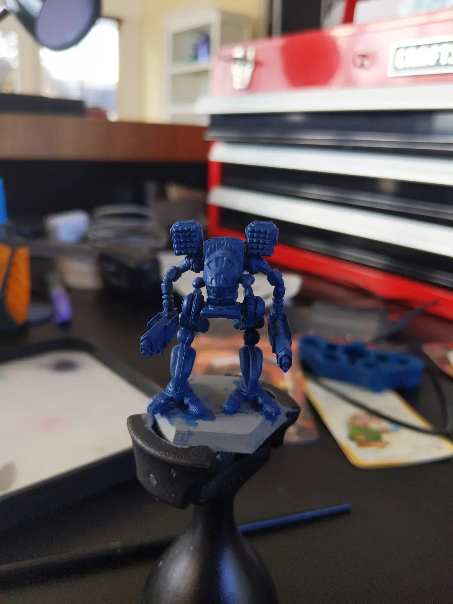 Blue mech figure on a stand, ready for painting. Red toolbox in the background.