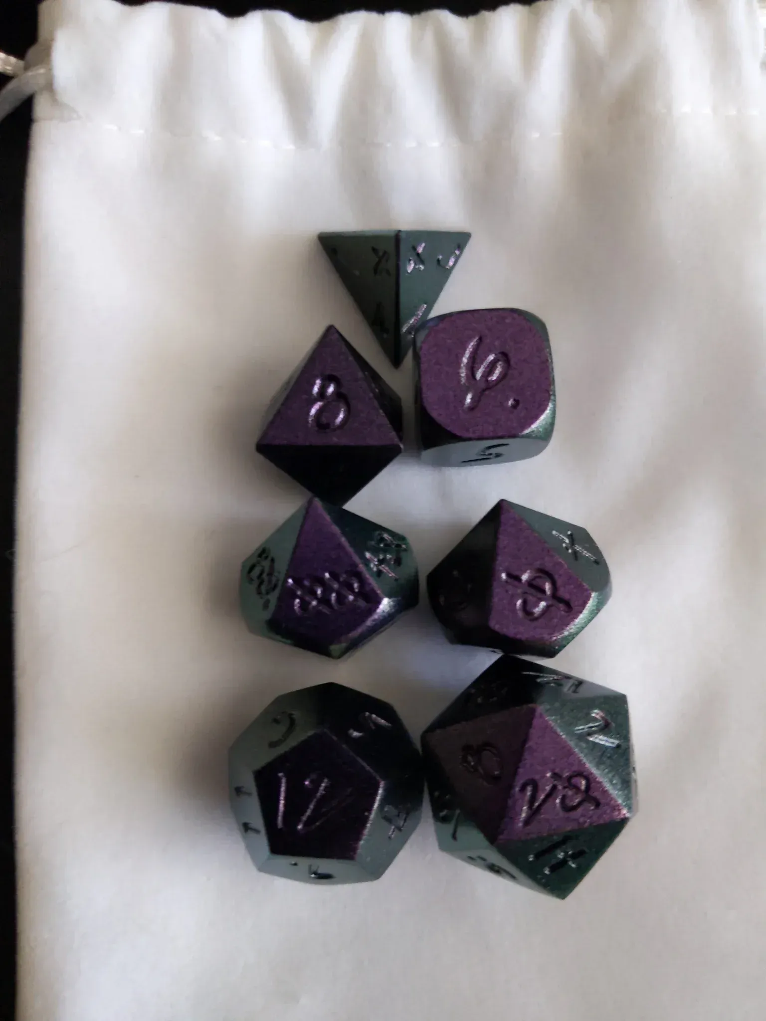 Set of dark green and purple polyhedral dice next to a white bag.