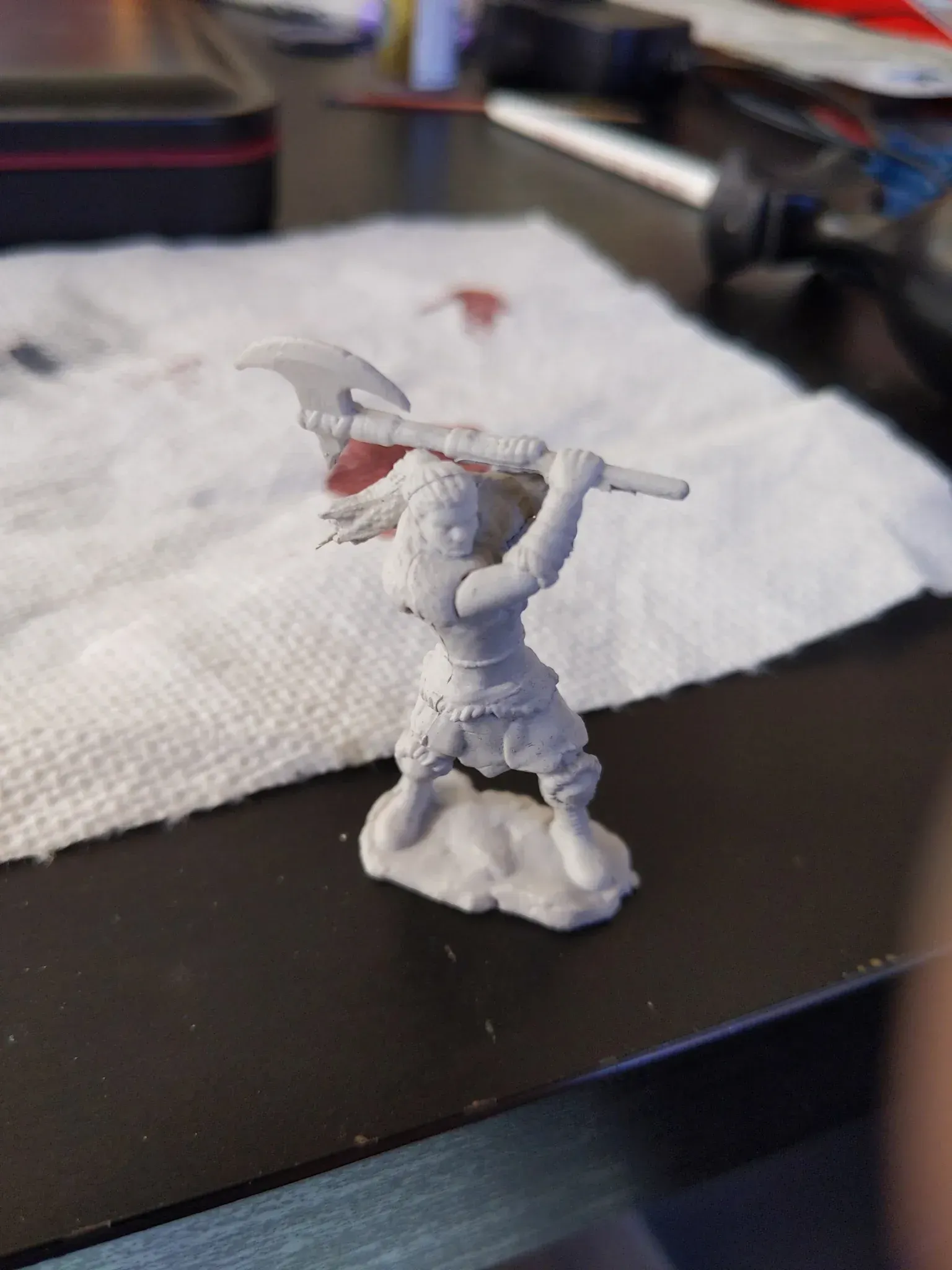 Miniature figurine of a warrior with an axe raised, poised on a rock base.