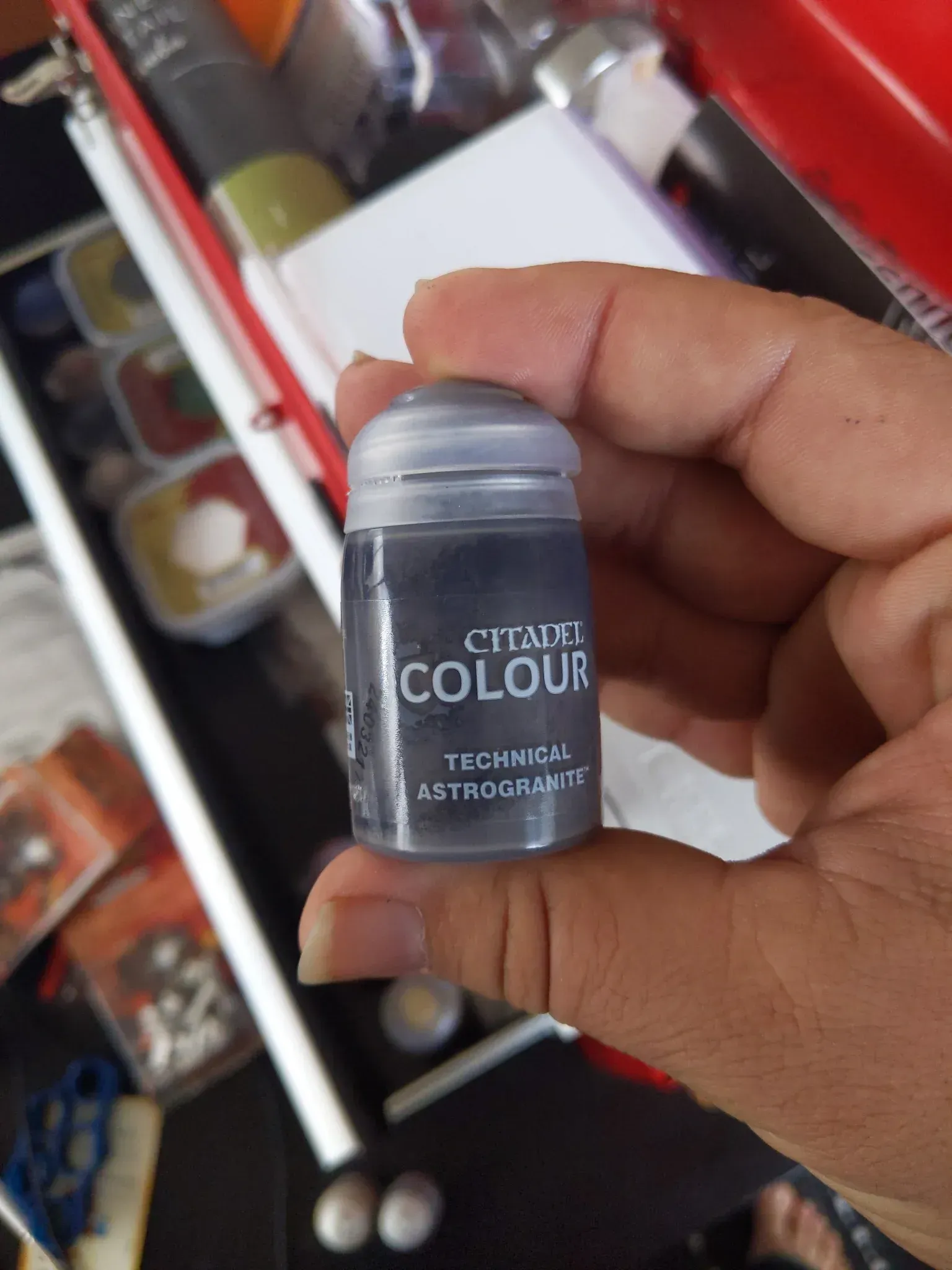 A person's hand holding a small, gray Citadel paint pot.  The label reads 