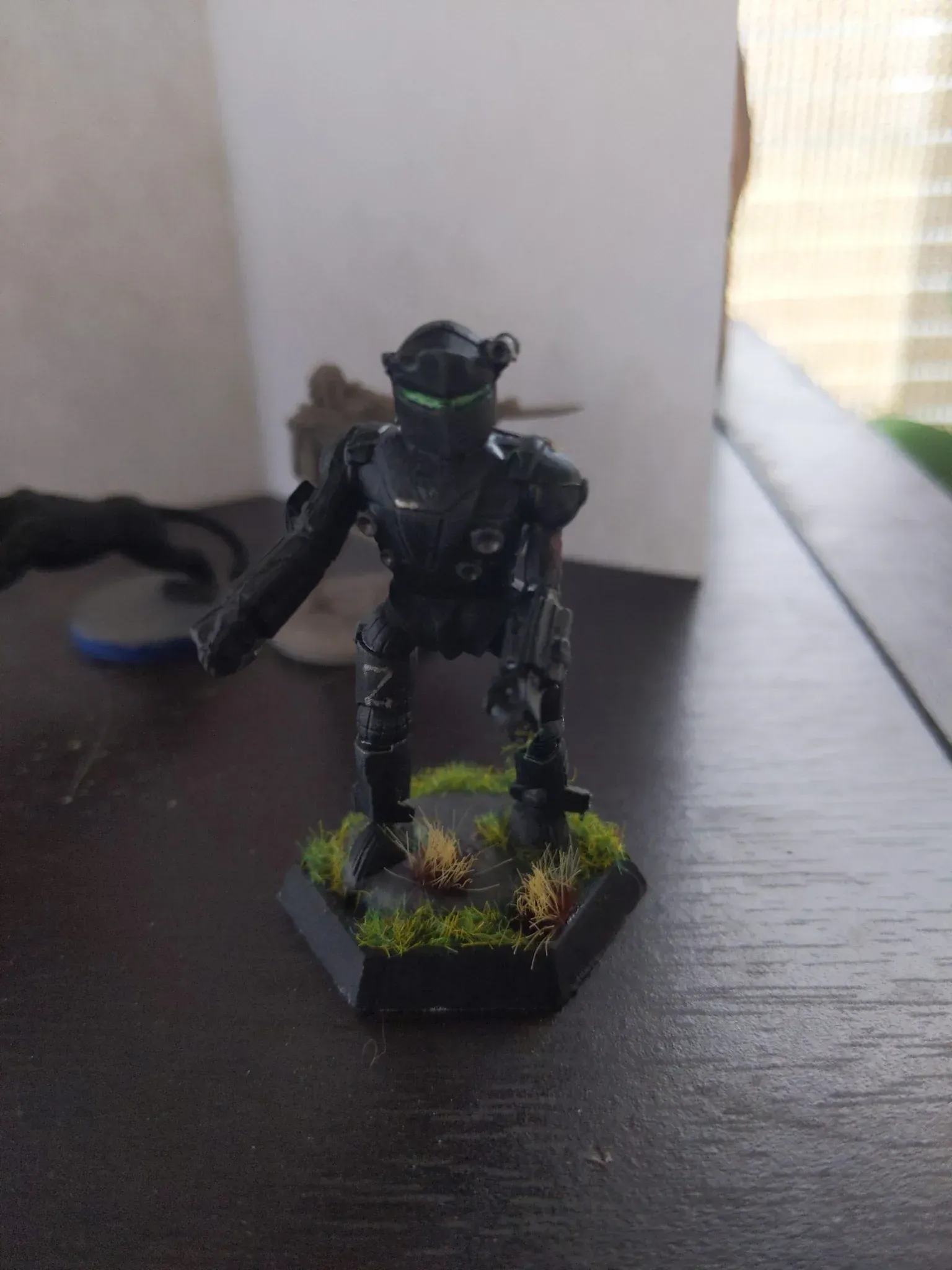 Black mech warrior model with glowing green eyes, standing on a hexagonal base with grass detail.