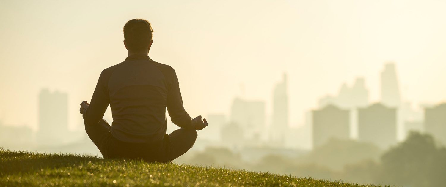 A man is sitting in a lotus position in front of a city skyline.