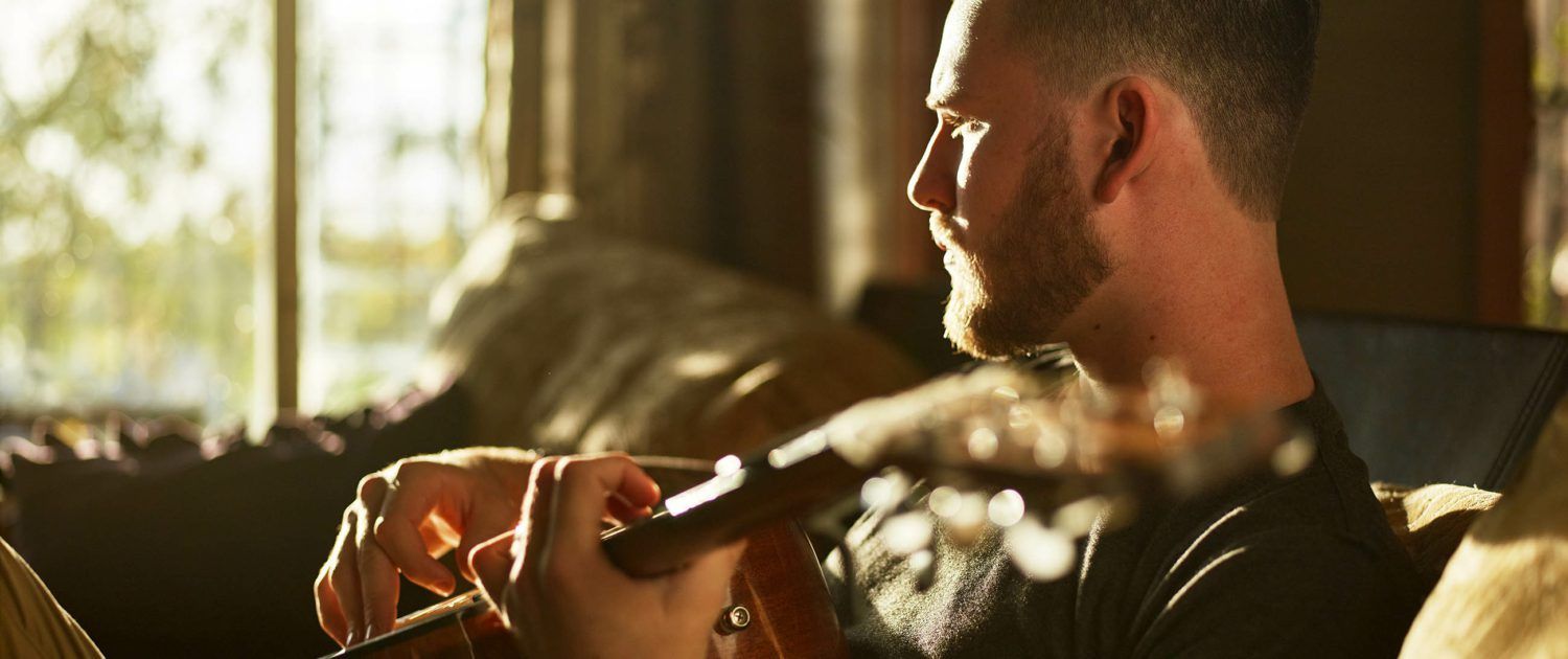 A man is sitting on a couch playing a guitar.