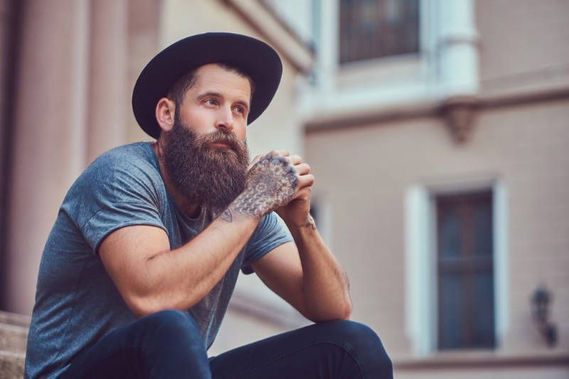 A man with a beard and a hat is sitting on a staircase.