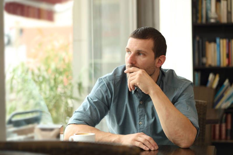 A man is sitting at a table with his hand on his chin and looking out the window.