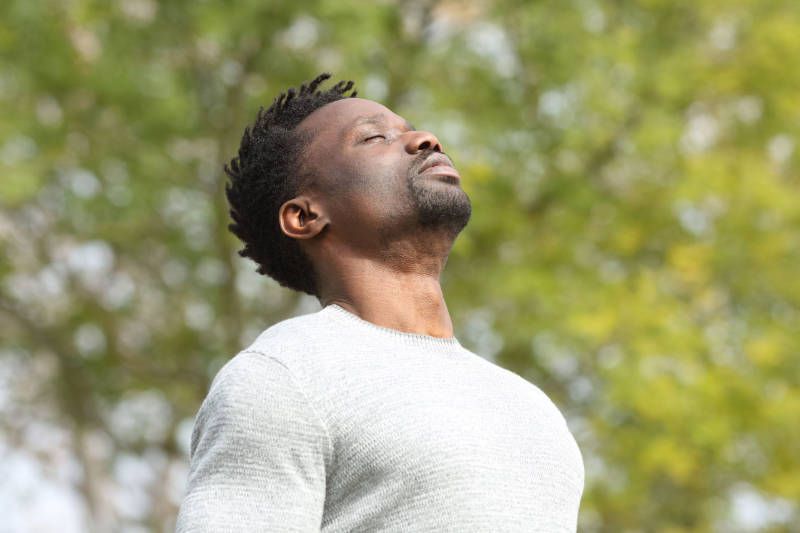 A man is taking a deep breath of air in a park.