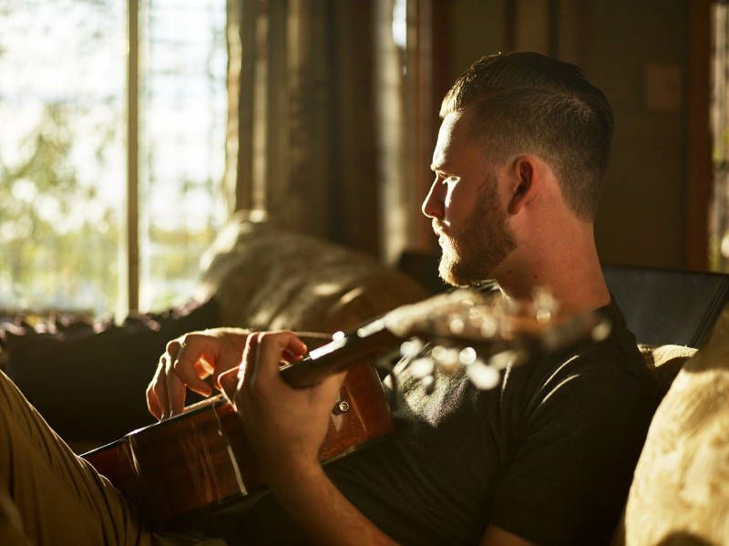 A man is sitting on a couch playing a guitar.