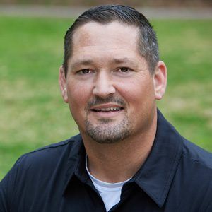 A man with a beard is wearing a black shirt and smiling for the camera.