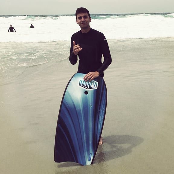 A man is holding a boogie board on the beach