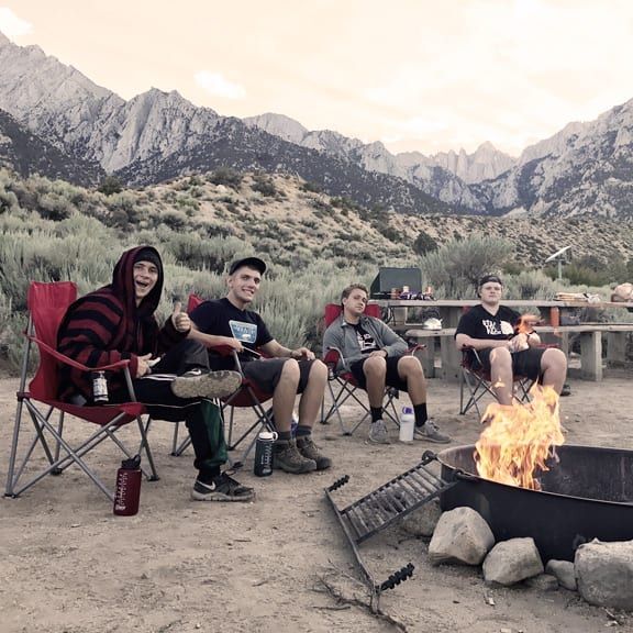 A group of people sitting around a fire pit with mountains in the background