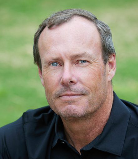 A man with a beard and blue eyes is wearing a black shirt and looking at the camera.