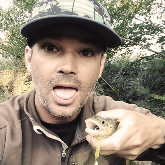 A man wearing a hat is holding a fish in his hand