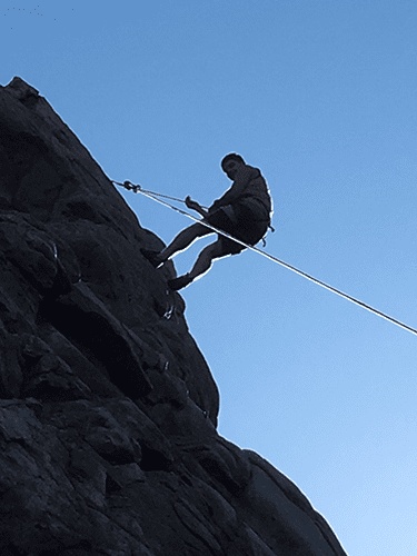 A man is climbing up a rock with a rope