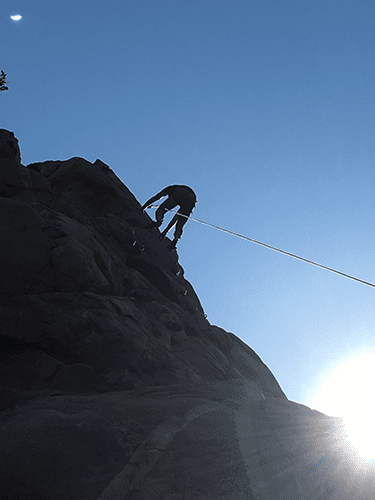 A person is climbing up a rock with a rope