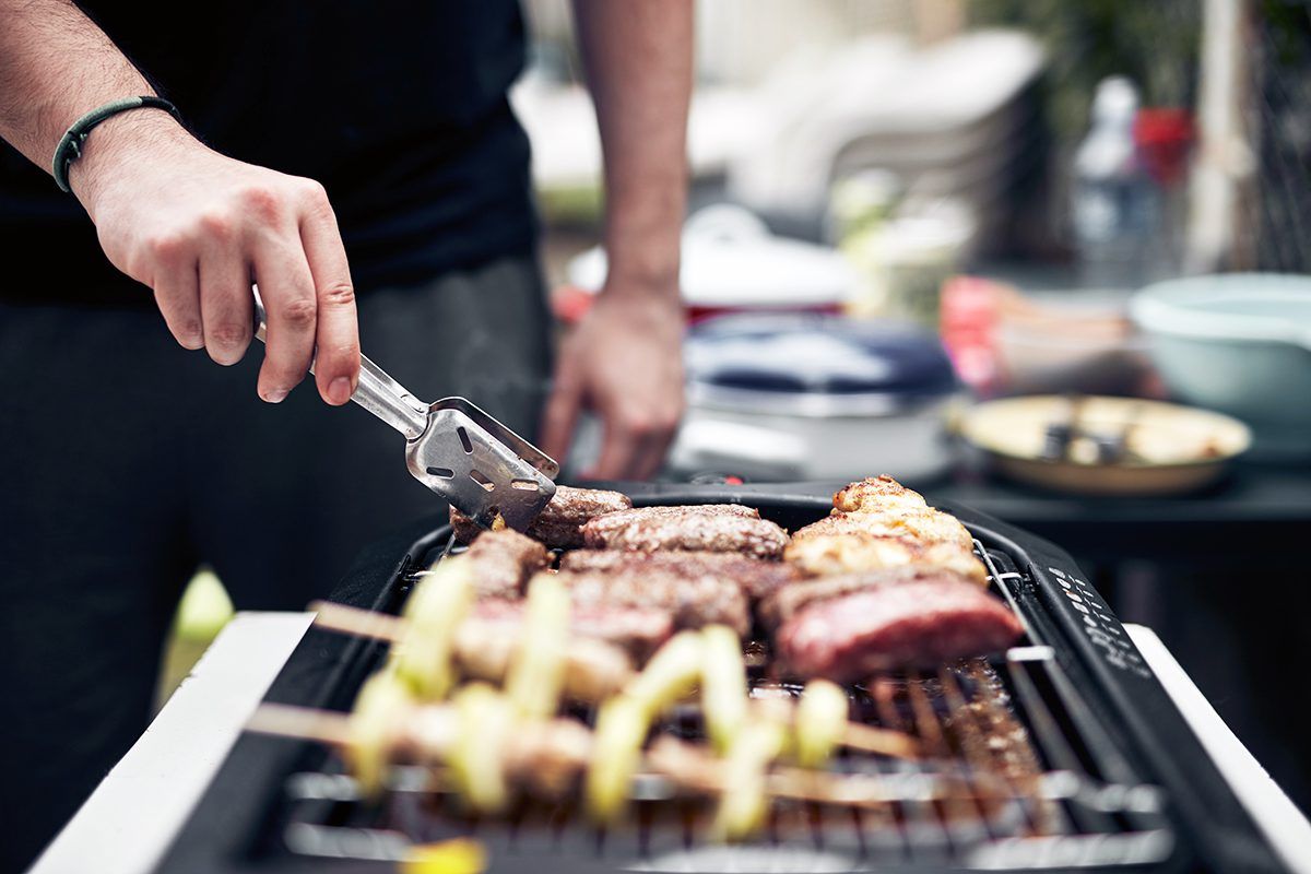 A man is grilling meat and vegetables on a grill.