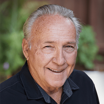 An older man in a black shirt is smiling for the camera.