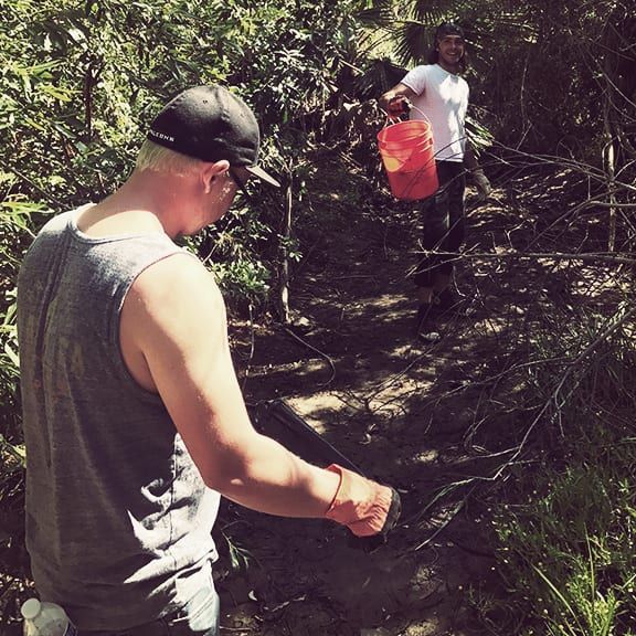 A man in a gray tank top is standing in the woods