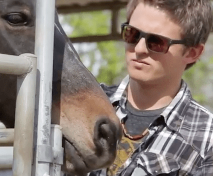 A man wearing sunglasses is petting a horse behind a fence